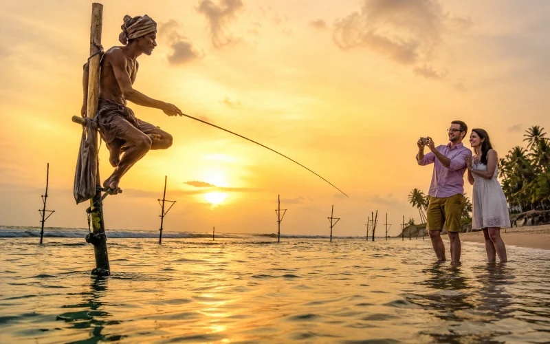 Close-up of a Sri Lankan stilt fisherman balanced on his traditional pole at sunset while tourists take photos in Koggala